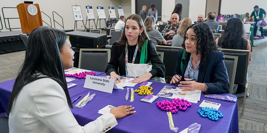 Three SOT Annual Meeting attendees speak at a Louisiana State University table. 