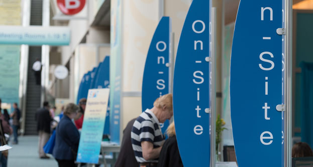 On the right-hand side of the image is a series of vertical signs that read On-Site. People stand intermittently between these signs. On the left is a long lobby space.