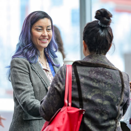 An individual is smiling as they greet another individual standing in front of them.