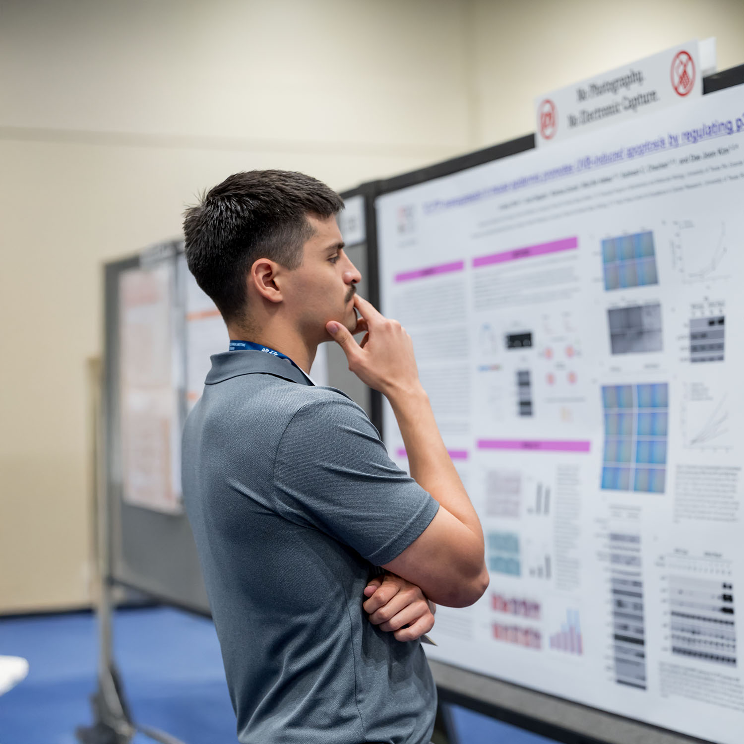 An individual has their hand on their chin while looking at a poster board.