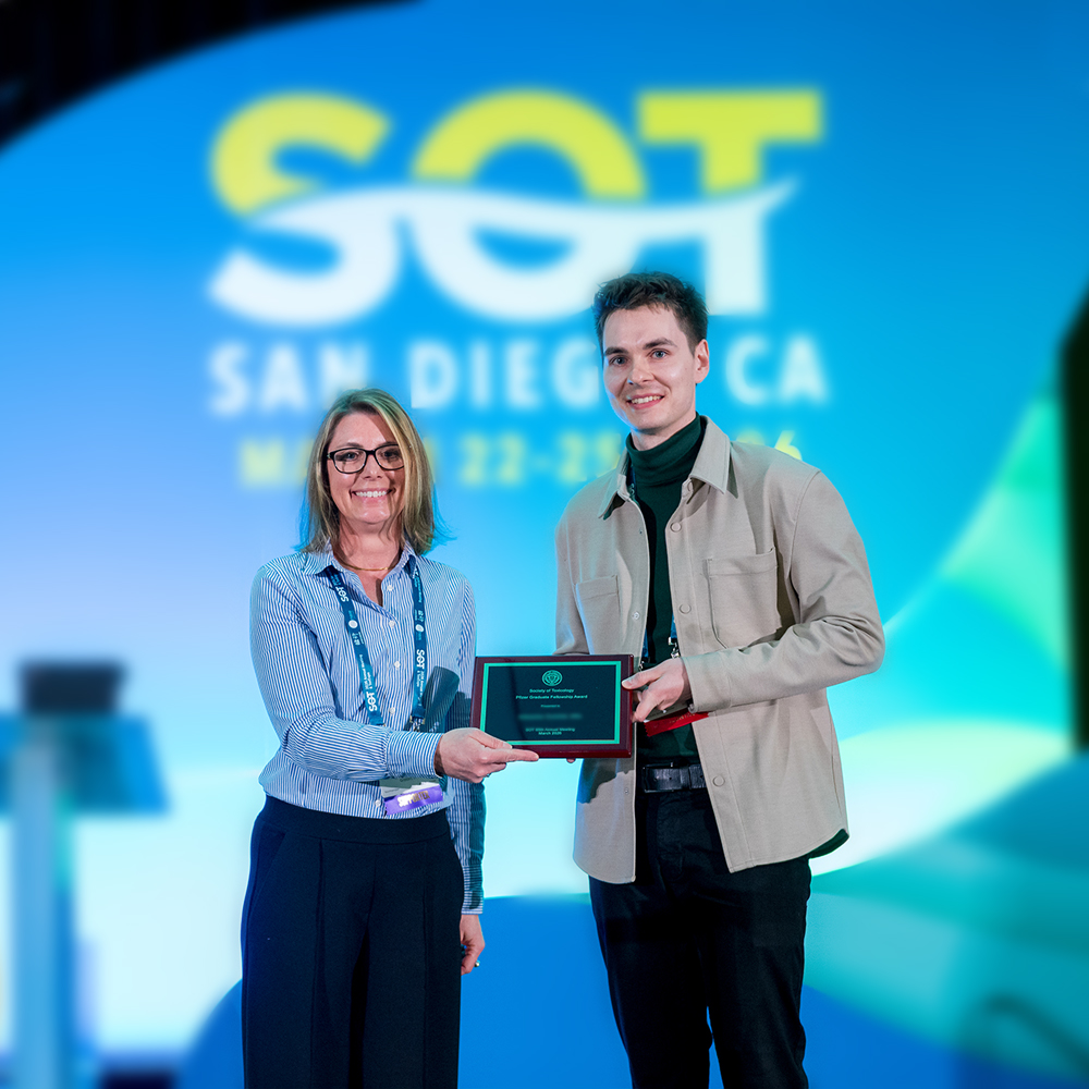 Two SOT Annual Meeting attendees stand on stage holding an award plaque. 