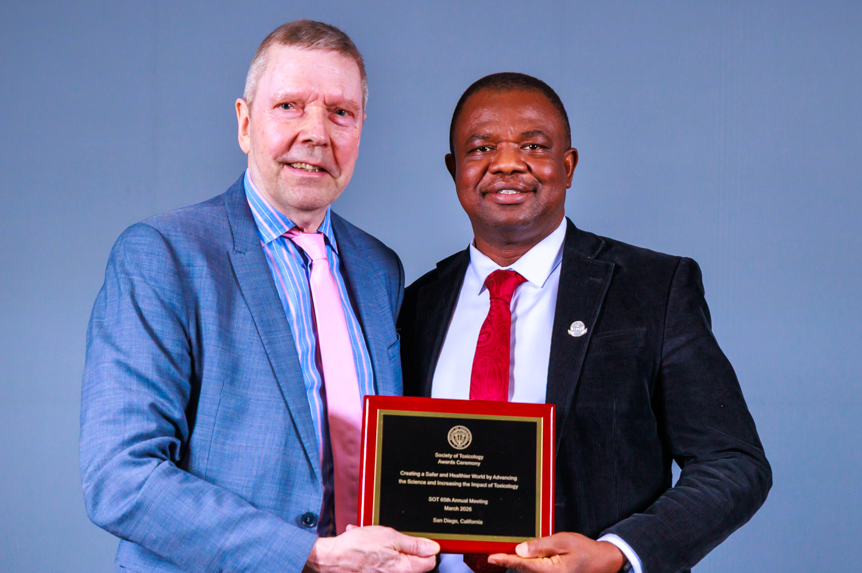 Two SOT Annual Meeting attendees stand together holding an award plaque in front of a blue backdrop. 