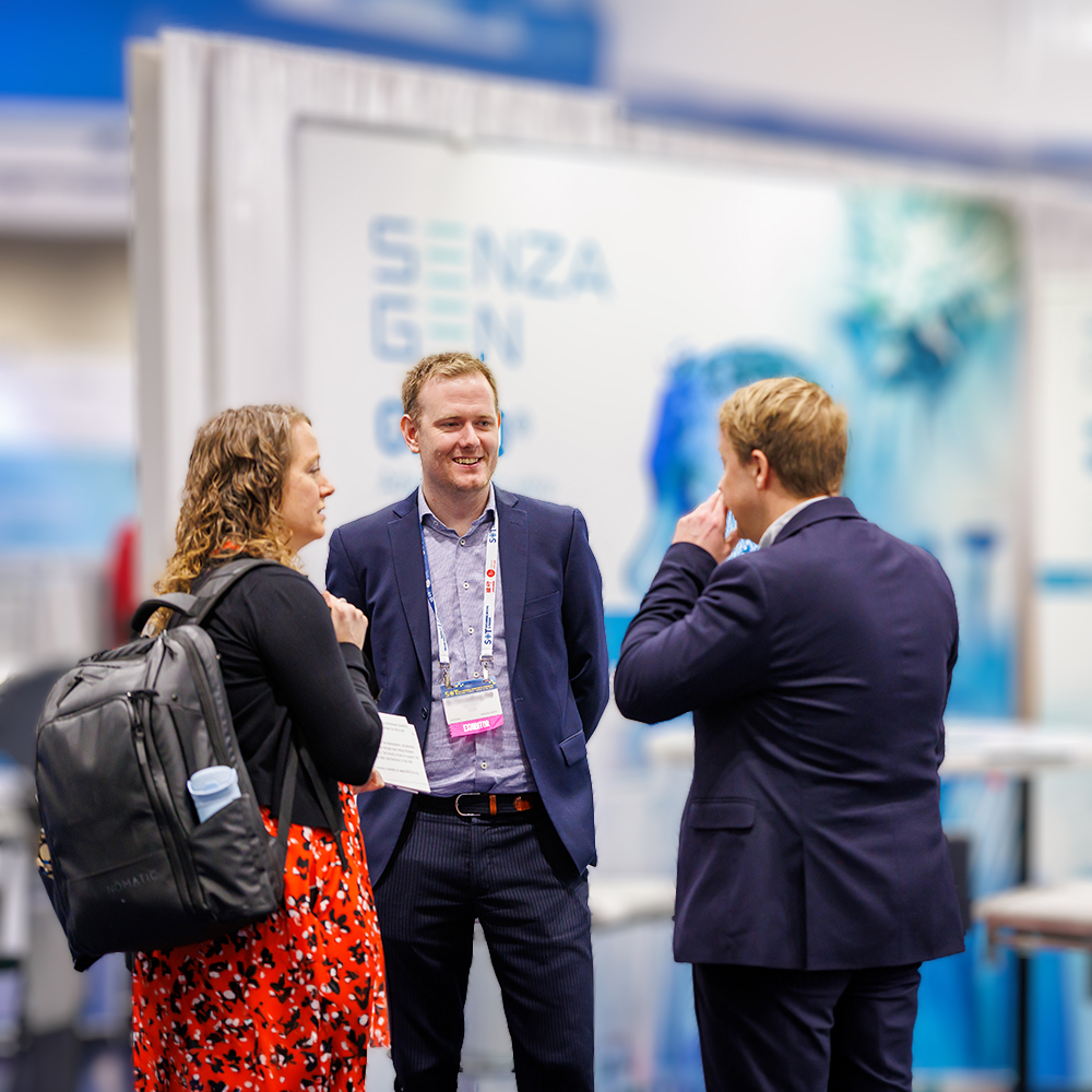 A smiling attendee talks with two others in the ToxExpo hall.