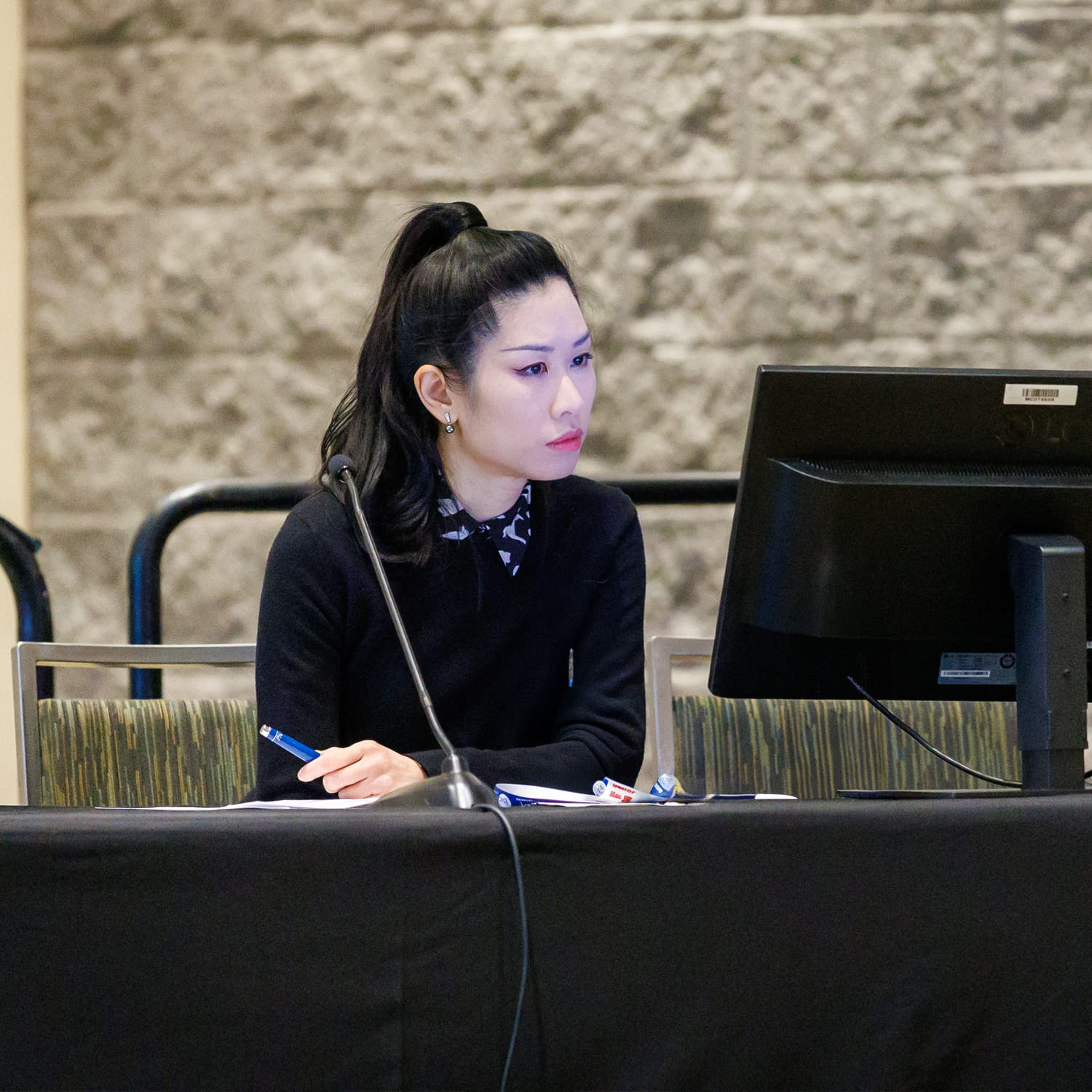 An individual sits at a table and is looking at a computer monitor.