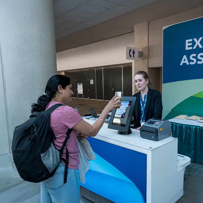 An individual stands in front of a kiosk. They are holding their phone in front of an electronic device.