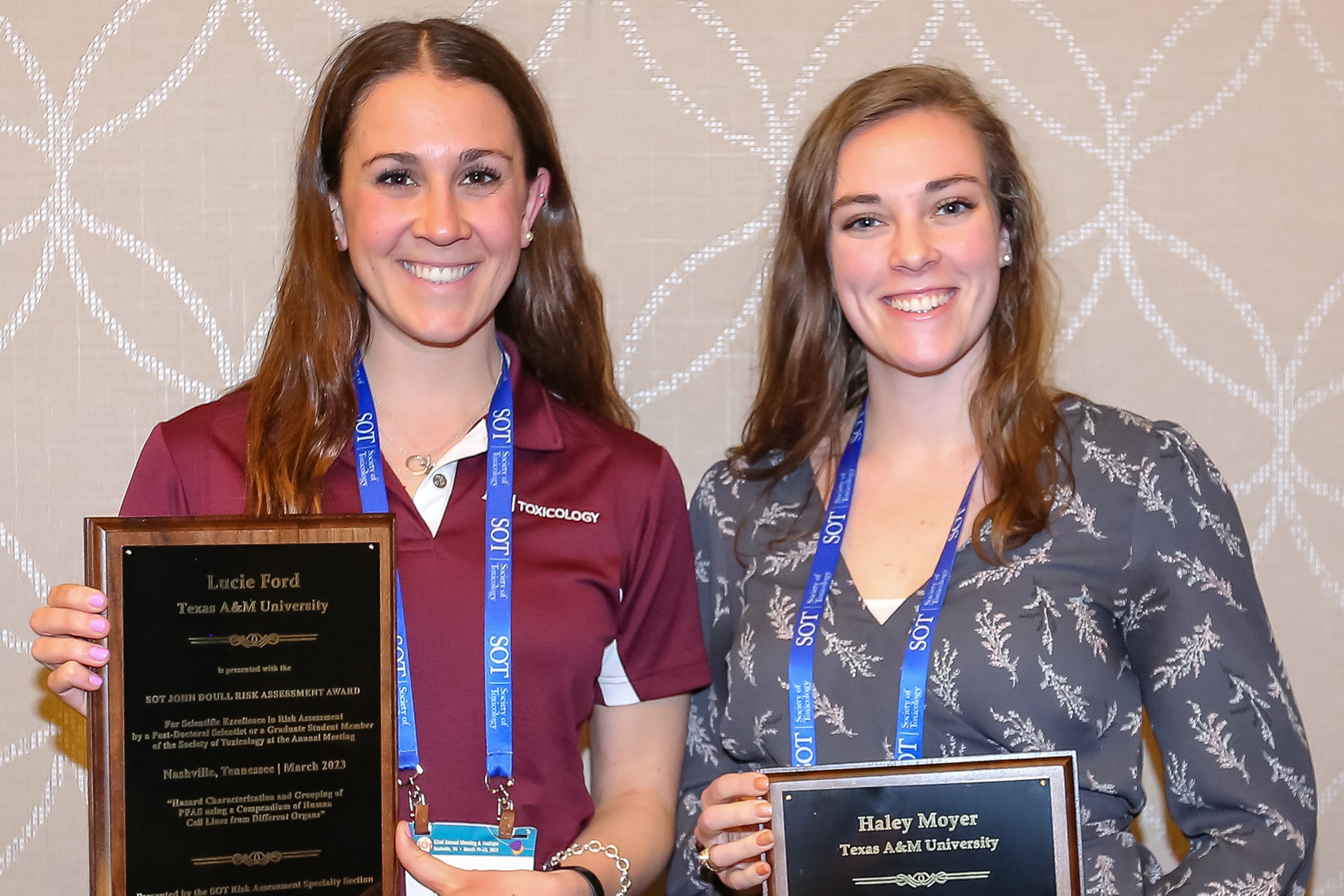 Two women are standing beside each other both holding award plaques. They are both facing forward and smiling at the camera.