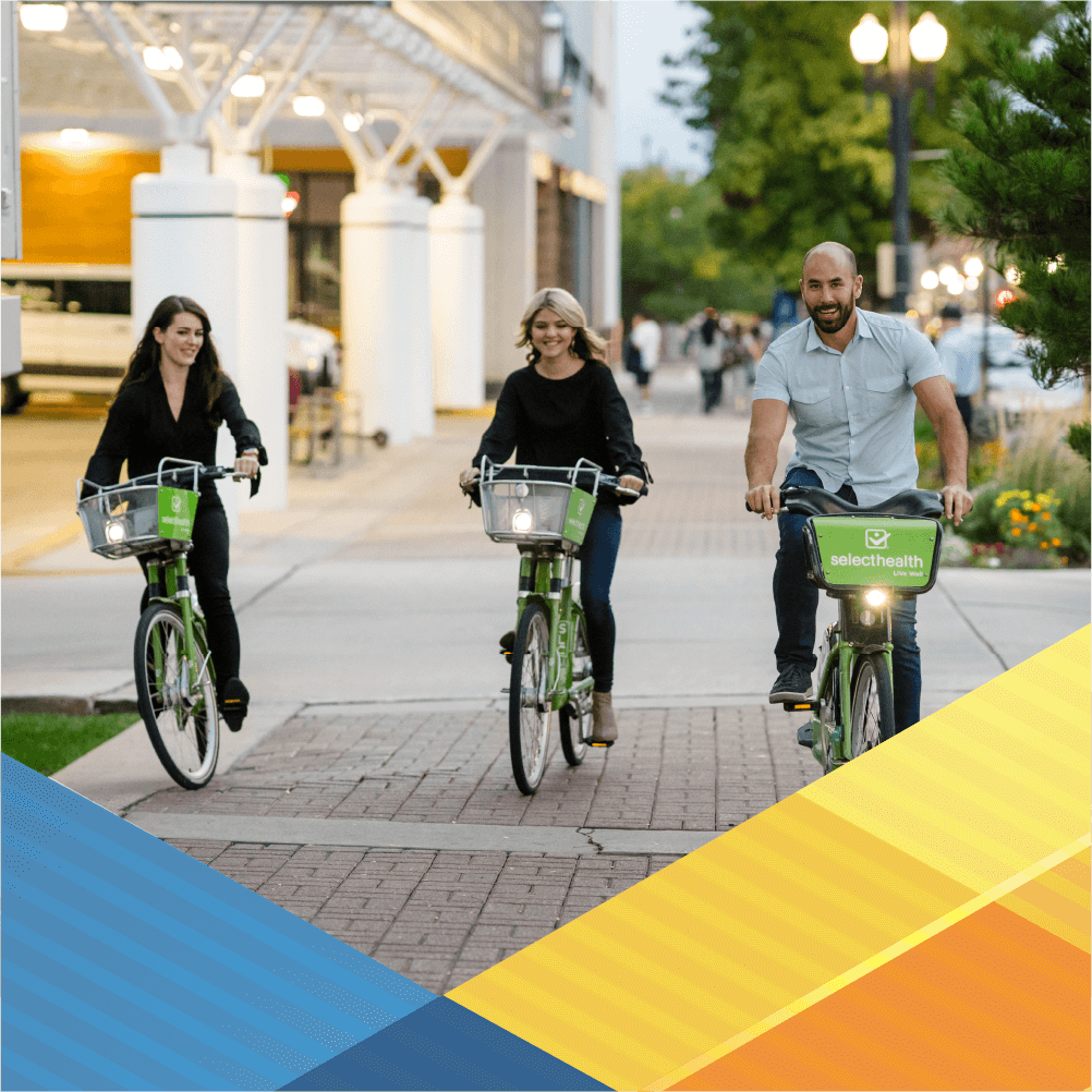 Three individuals are riding lime green bikes down a city sidewalk toward the camera.