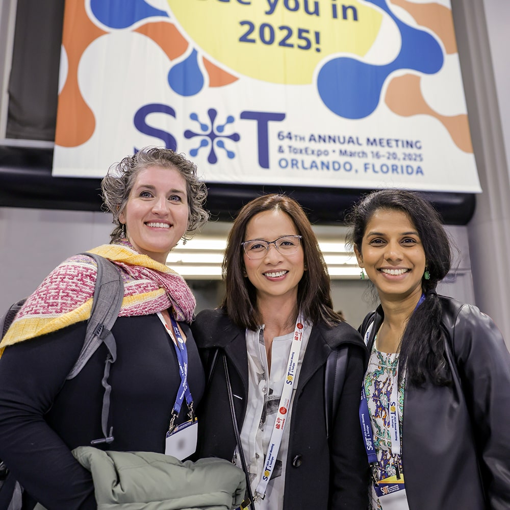 Three individuals stand next to each other. They are looking at the camera and smiling.