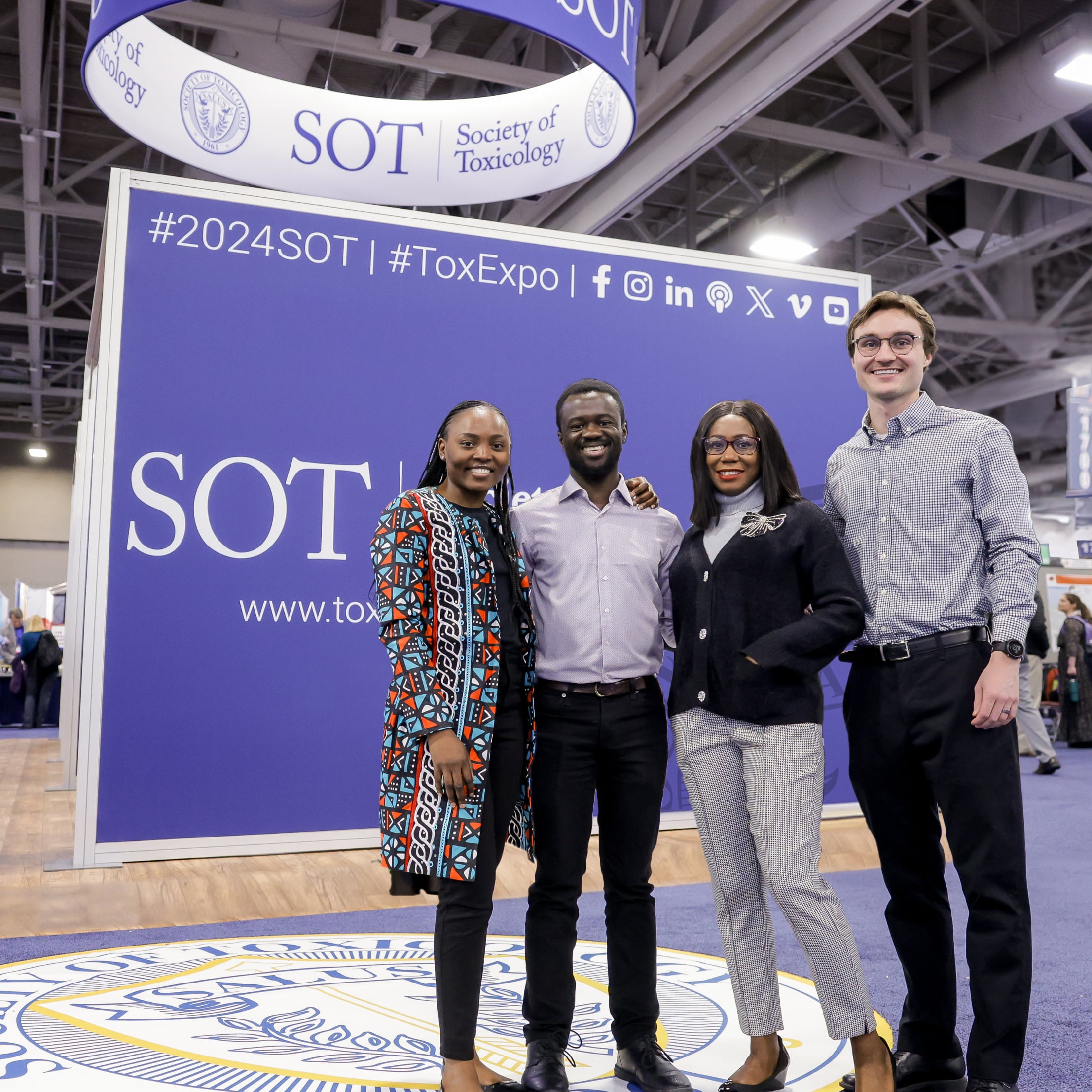 Four individuals stand next to each other. They are posed and smiling at the camera.