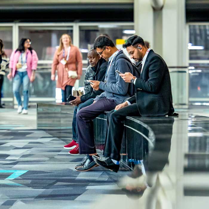 Individuals sit on a low, decorative wall. They are seen in profile looking at mobile devices.