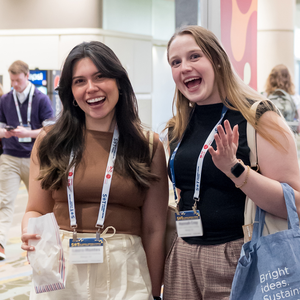 Two individuals stand shoulder-to-shoulder. They are looking at the camera and smiling.