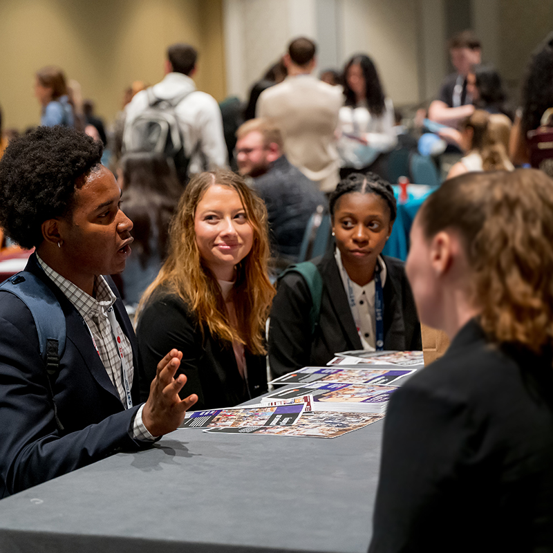Students are engaged in conversation around a table at a career event, with informational brochures spread out in front of them.