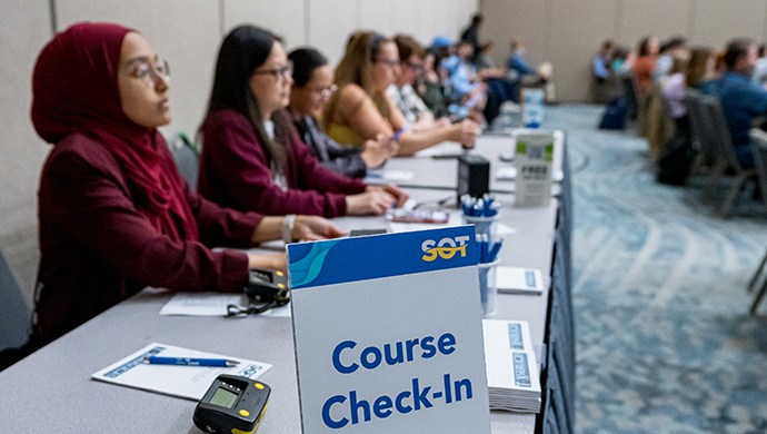 Individuals are seated behind a long, skirted table. A sign at the edge of the table reads Course Check-In. 