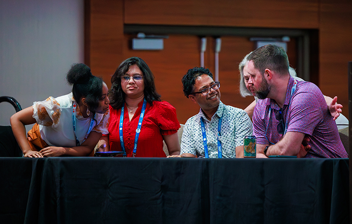 Five SOT Annual Meeting attendees sit at a panel table on stage, speaking with one another. 